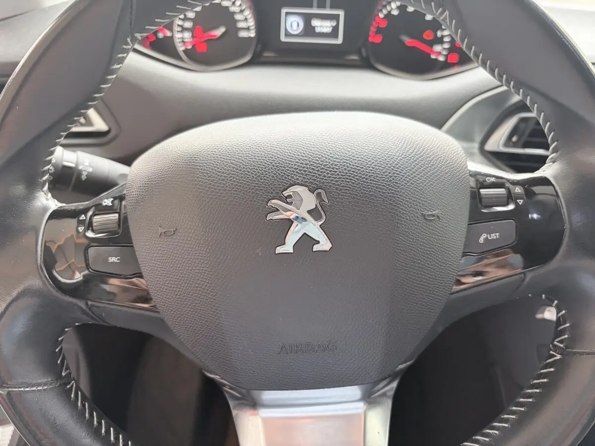 Volant cuir noir multi-fonctions Peugeot 308 BlueHDi 130 S&S Allure, avec logo lion et commandes intégrées.