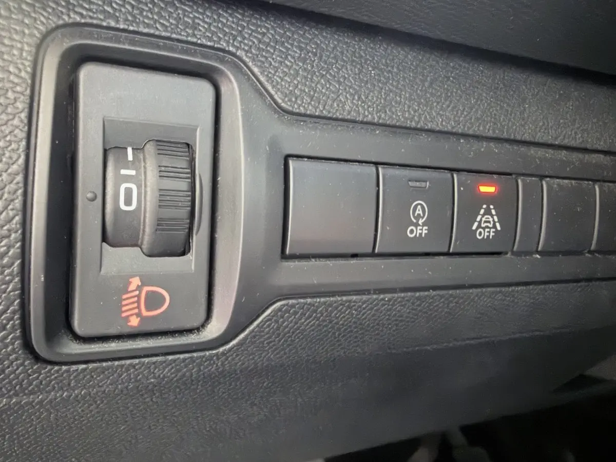 Gros plan sur les commandes noires du tableau de bord de la Peugeot 308 gris foncé, avec témoin lumineux rouge allumé.