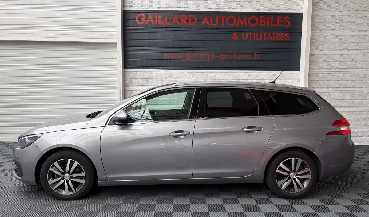 Profil côté gauche d'une Peugeot 308 SW gris foncé, vue en intérieur de garage avec jantes alliage et vitres teintées.
