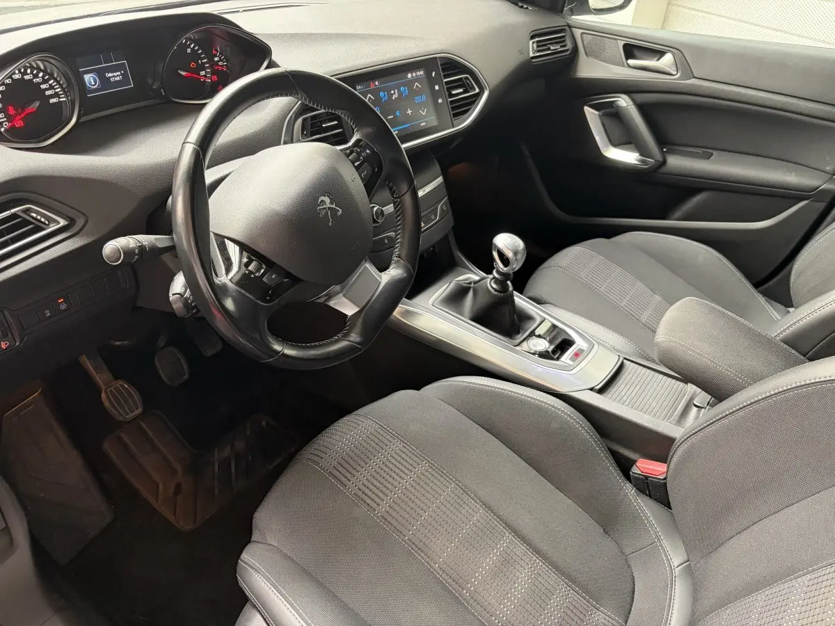 Vue intérieure côté conducteur de la Peugeot 308 gris foncé, volant cuir multifonctions et écran tactile central visible.
