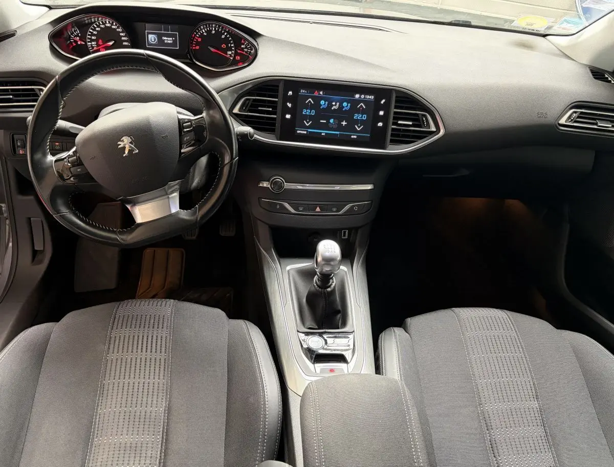 Vue intérieure avant de la Peugeot 308 gris foncé, volant cuir multifonctions et écran tactile central visible.