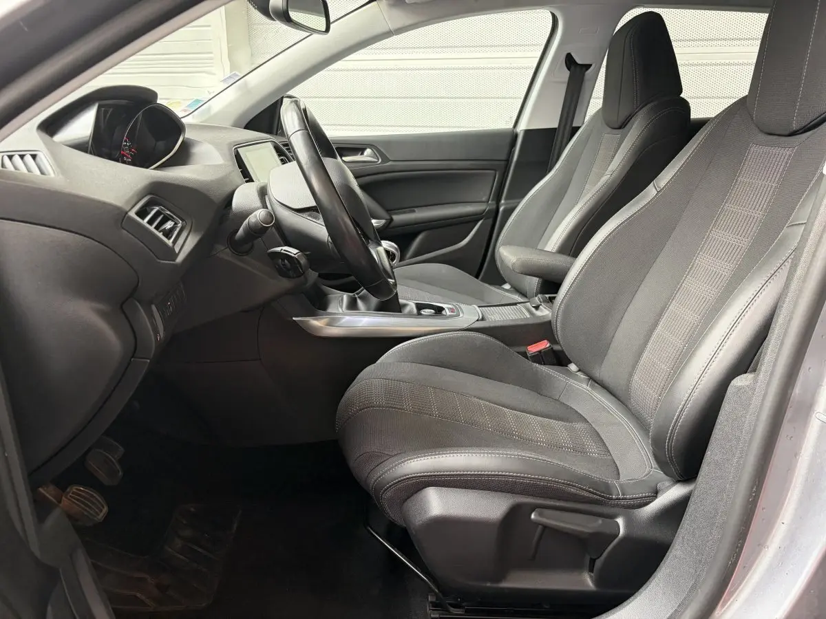 Vue intérieure côté conducteur de la Peugeot 308 gris foncé, montrant sièges tissu et volant cuir multifonctions.