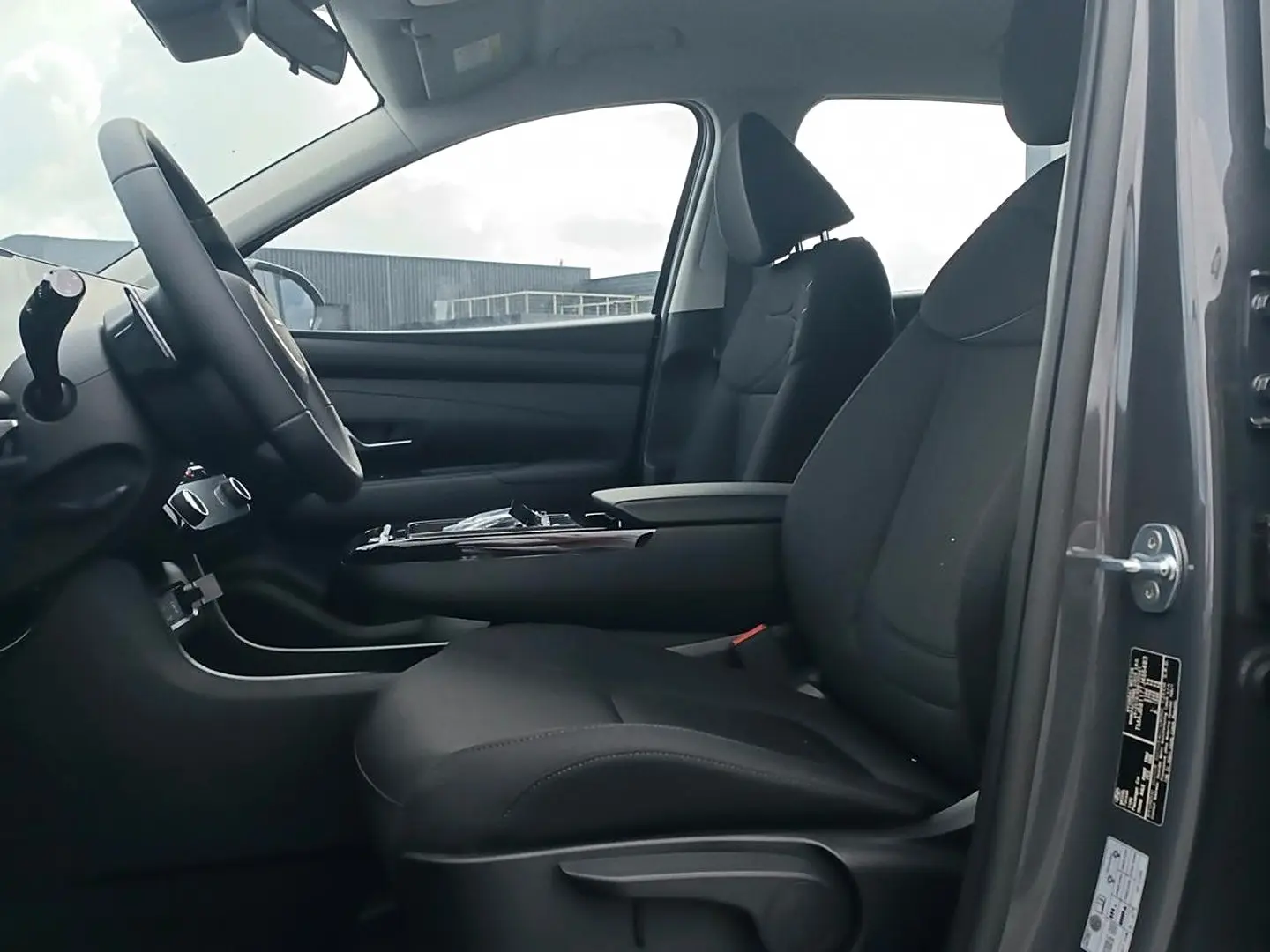 Vue intérieure côté conducteur du Hyundai Tucson gris ecotronique, montrant les sièges noirs et l'accoudoir central.