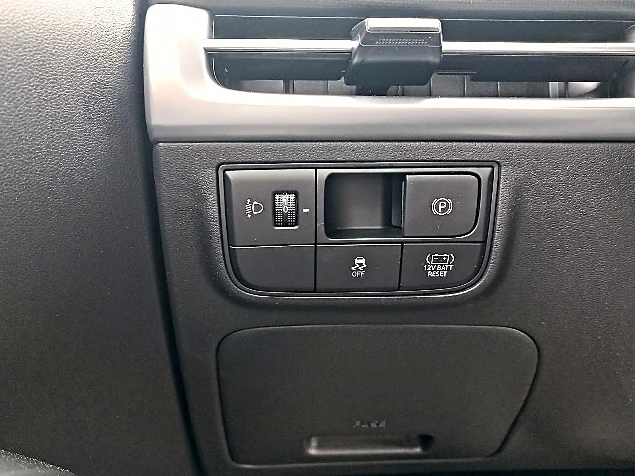 Gros plan sur les commandes noires du tableau de bord du Hyundai Tucson gris, avec réglage des phares et frein de stationnement électrique.
