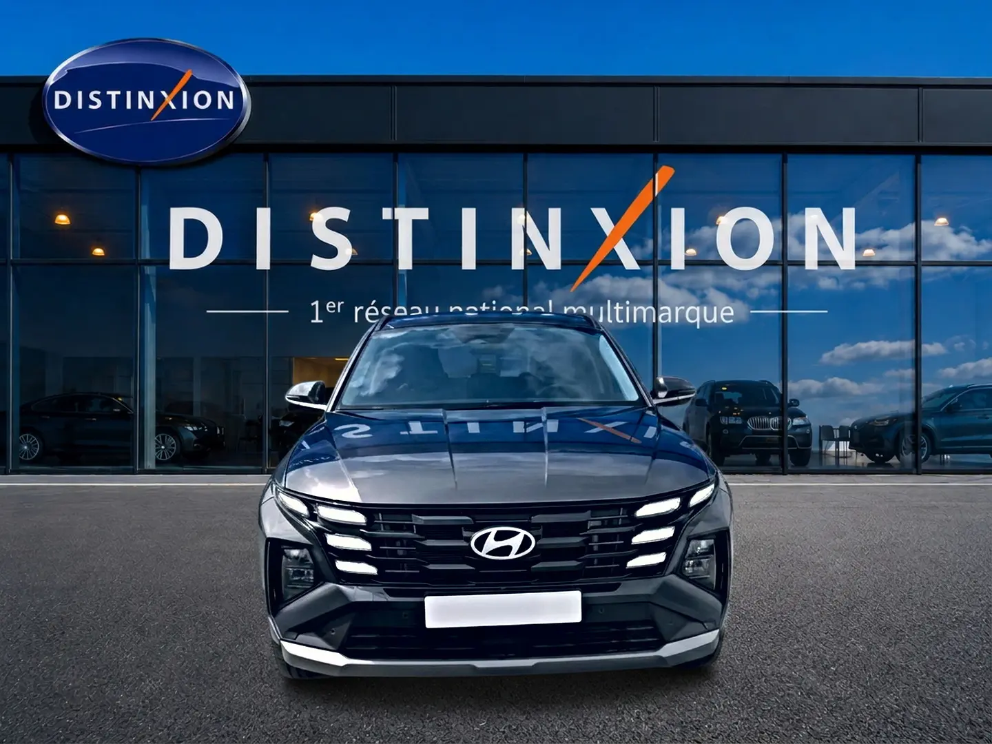 Vue frontale d’un Hyundai Tucson gris ecotronique avec calandre noire et feux LED allumés devant un showroom Distinxion.