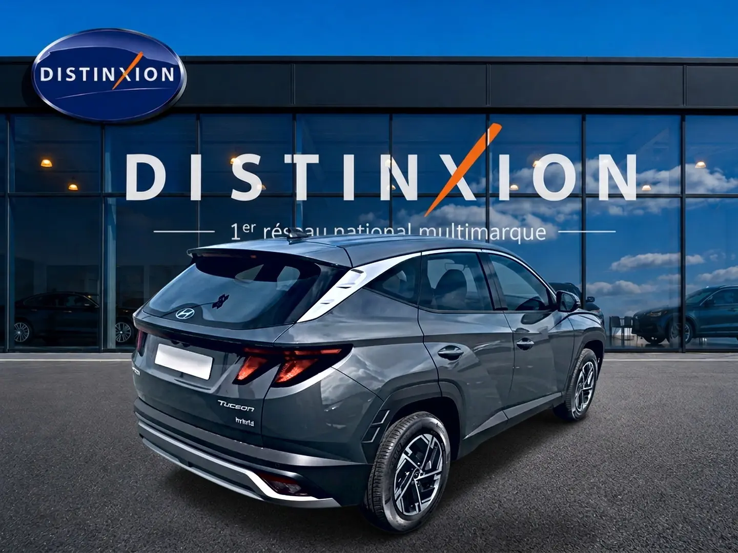 Vue 3/4 arrière droite du Hyundai Tucson gris ecotronique avec jantes alliage et vitres teintées devant un showroom Distinxion.