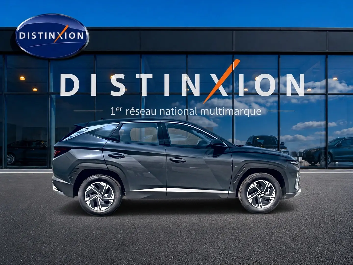 Hyundai Tucson 2026 gris ecotronique vu de profil côté gauche devant une vitrine Distinxion.