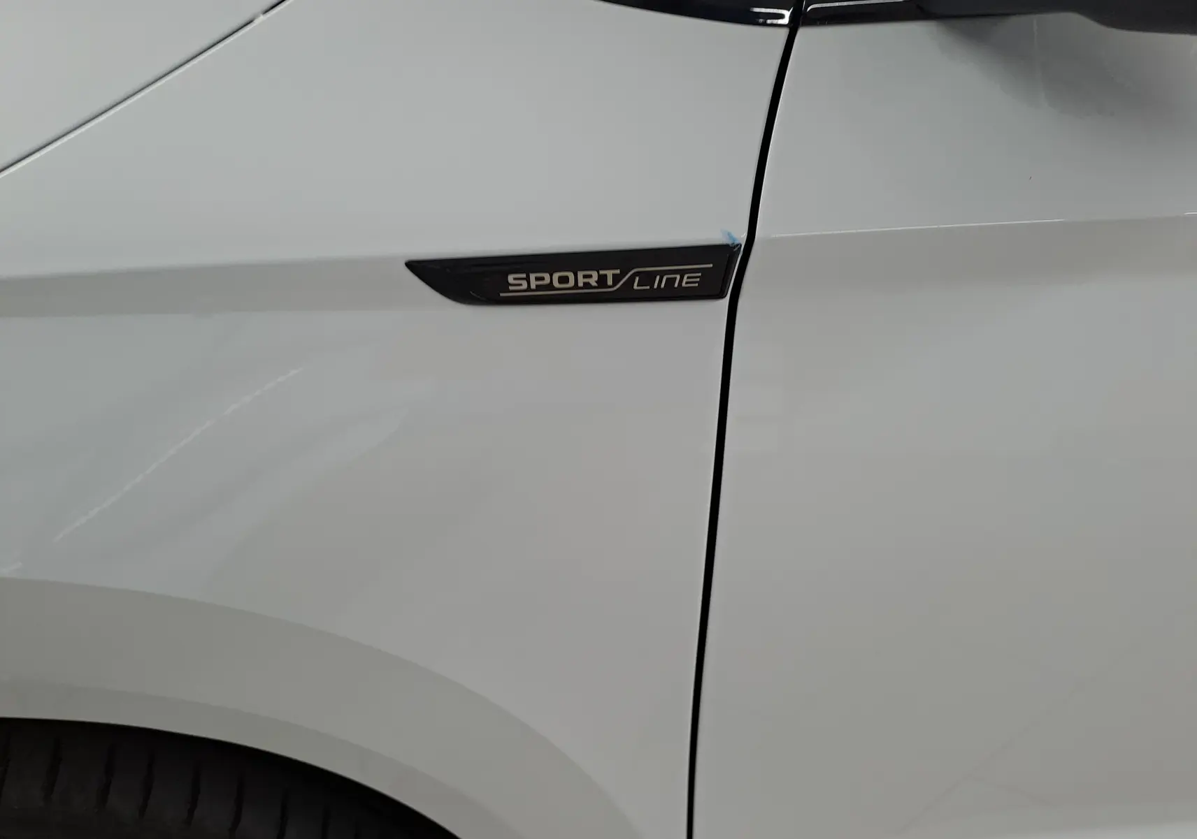 Gros plan sur l'aile avant gauche blanche lune du Skoda Karoq 2025 avec logo Sportline noir.