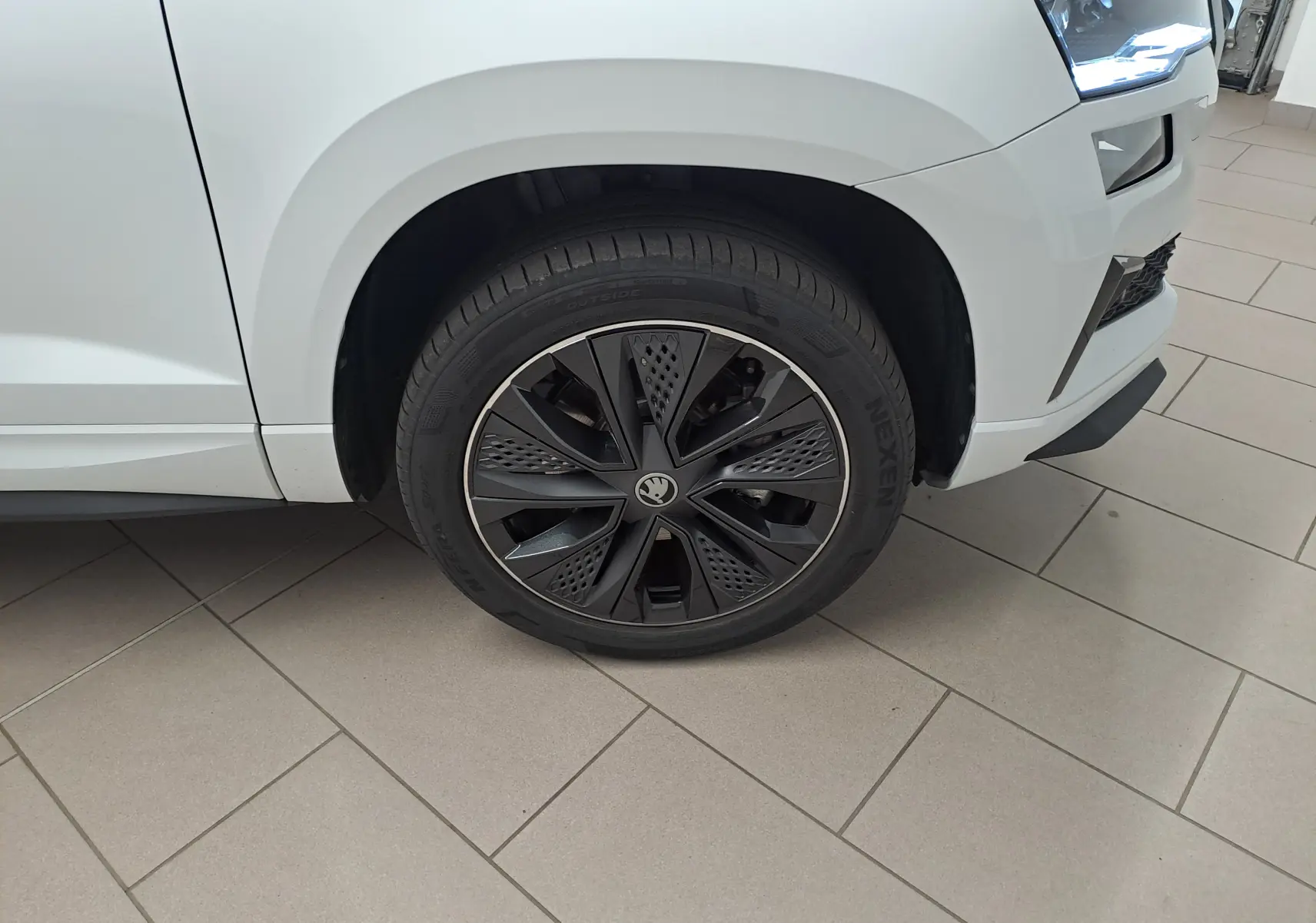 Gros plan sur la roue avant droite noire et argentée du Skoda Karoq blanc Lune, avec partie avant du véhicule visible.