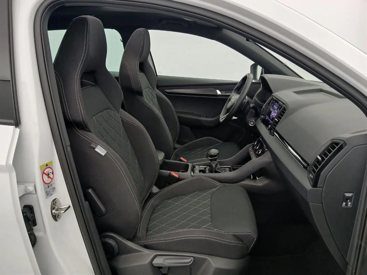 Vue intérieure côté conducteur du Skoda Karoq blanc lune 2025, sièges sport noirs avec surpiqûres blanches.