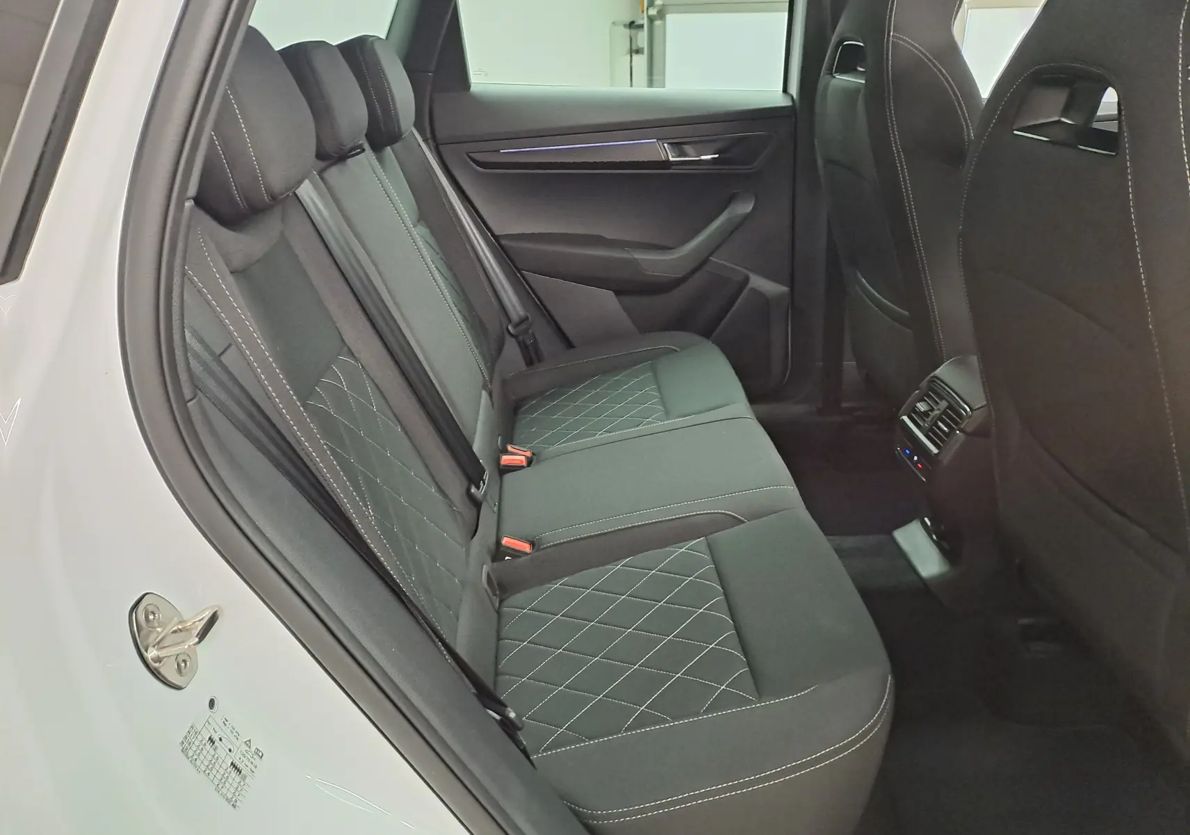 Vue intérieure côté gauche des sièges arrière noirs avec surpiqûres blanches du Skoda Karoq blanc lune 2025 Sportline.