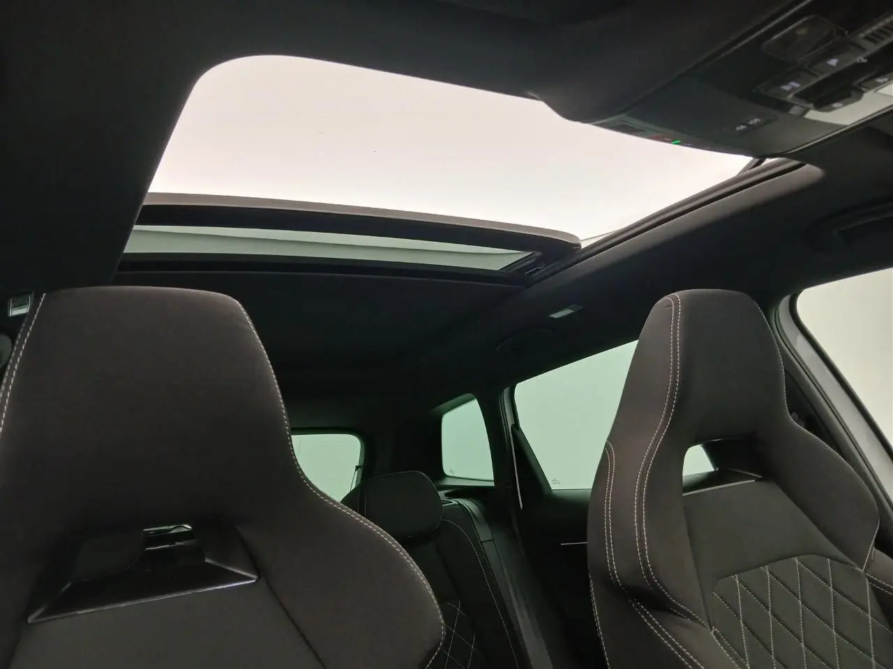 Vue intérieure du toit ouvrant panoramique en verre et des sièges avant noirs avec surpiqûres blanches du Skoda Karoq Blanc Lune.