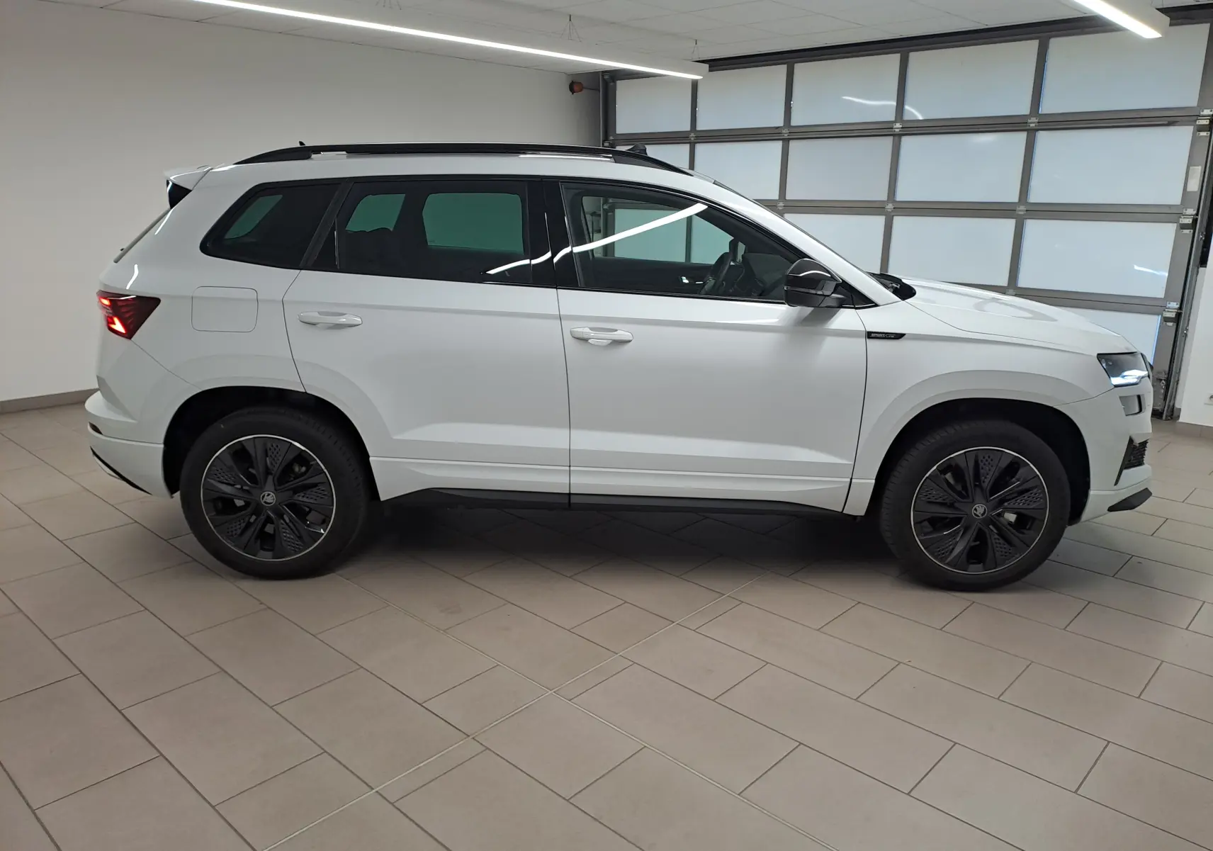 Vue de profil côté droit du Skoda Karoq blanc lune 2025 avec jantes noires et toit ouvrant panoramique.