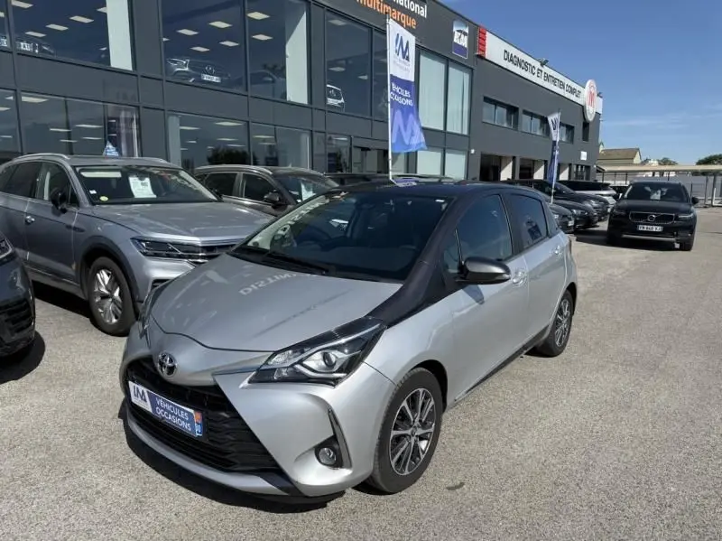 Toyota Yaris gris métal vue 3/4 avant droit, avec jantes alliage et calandre noire distinctive.