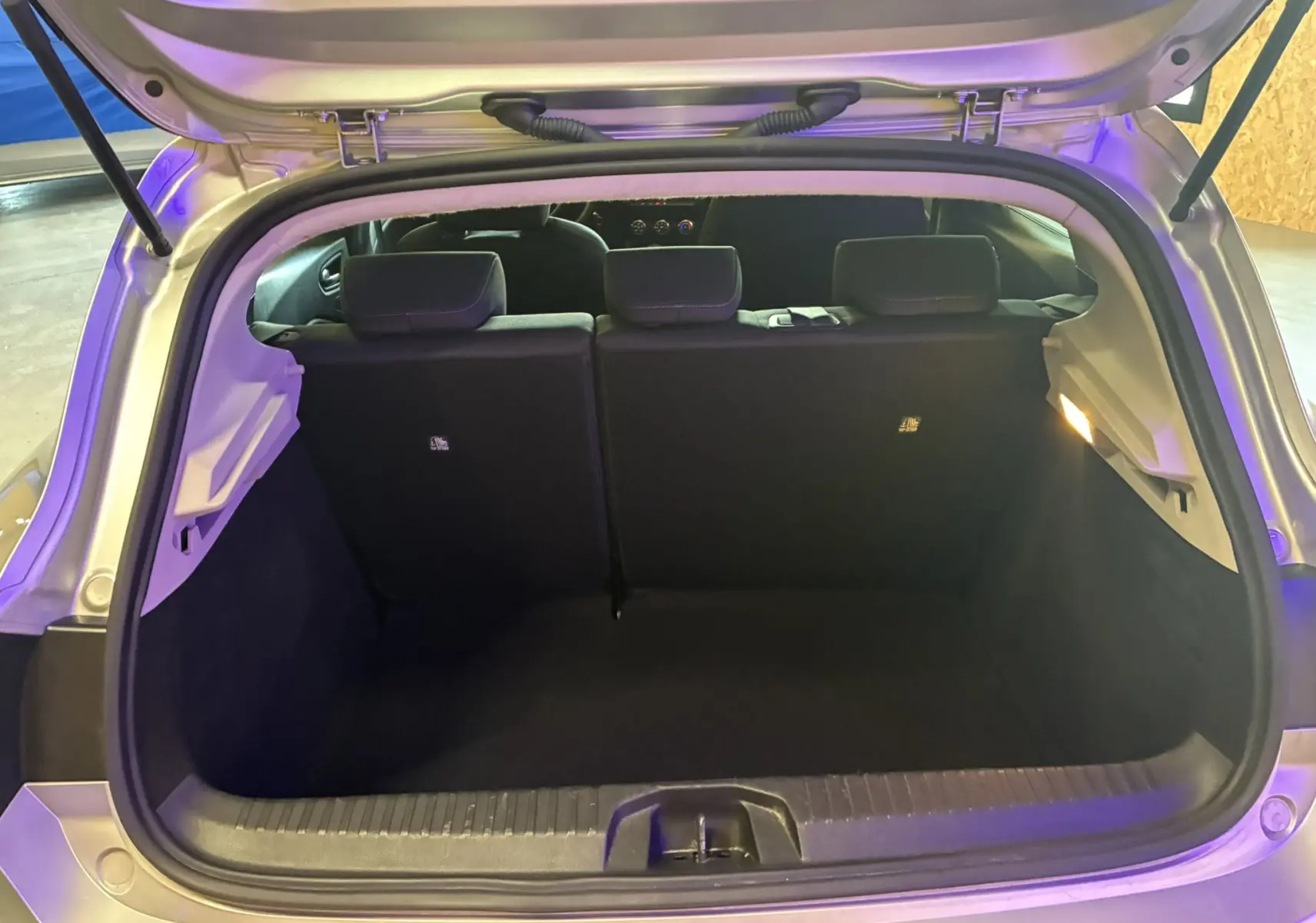 Coffre ouvert d'une Renault Clio 1.5 BlueDCI Business gris, vue arrière montrant l'espace de chargement et les sièges noirs.