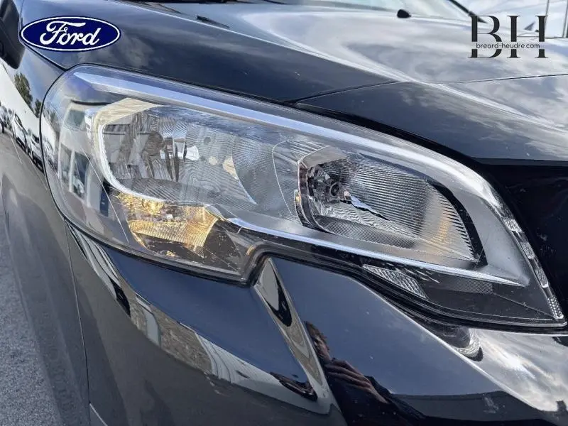 Gros plan sur le phare avant droit noir Perla Nera du Peugeot Expert Fourgon 2022, reflet du ciel nuageux visible.