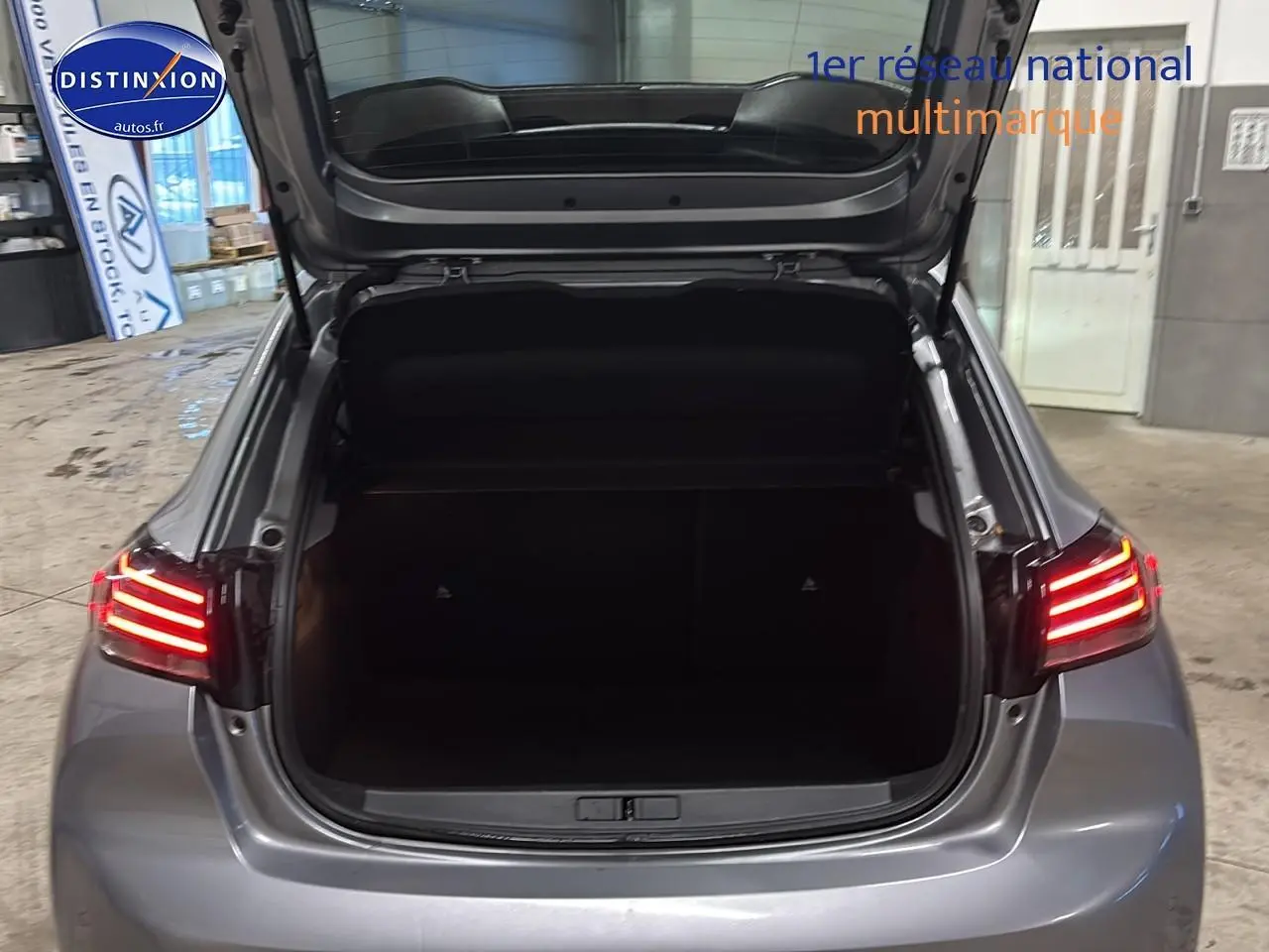 Vue arrière d'une Peugeot 208 gris artense avec coffre ouvert et feux arrière LED allumés dans un garage.