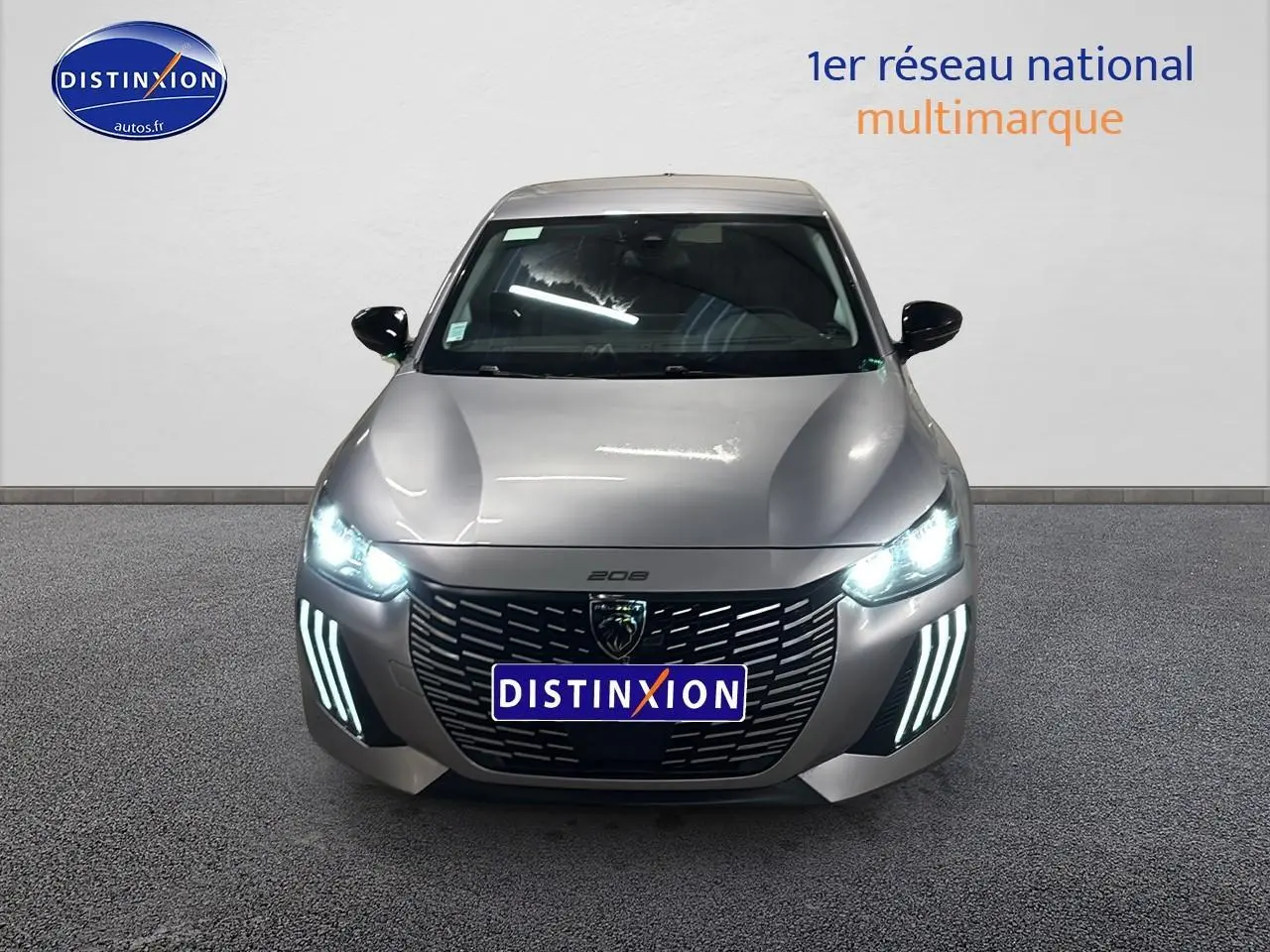 Vue avant d'une Peugeot 208 gris artense avec phares et feux diurnes LED allumés sur fond neutre.