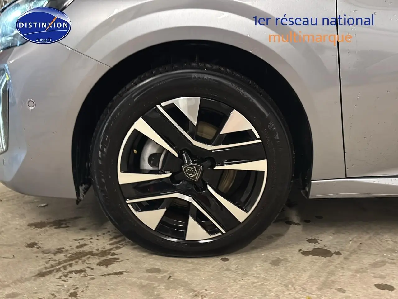 Gros plan sur la roue avant gauche avec jante alu bicolore du Peugeot 208 gris Artense 2025.