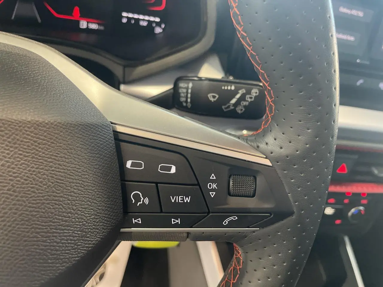 Gros plan sur le volant sport cuir noir perforé avec surpiqûres rouges du SEAT Arona 2024, boutons multifonctions visibles.