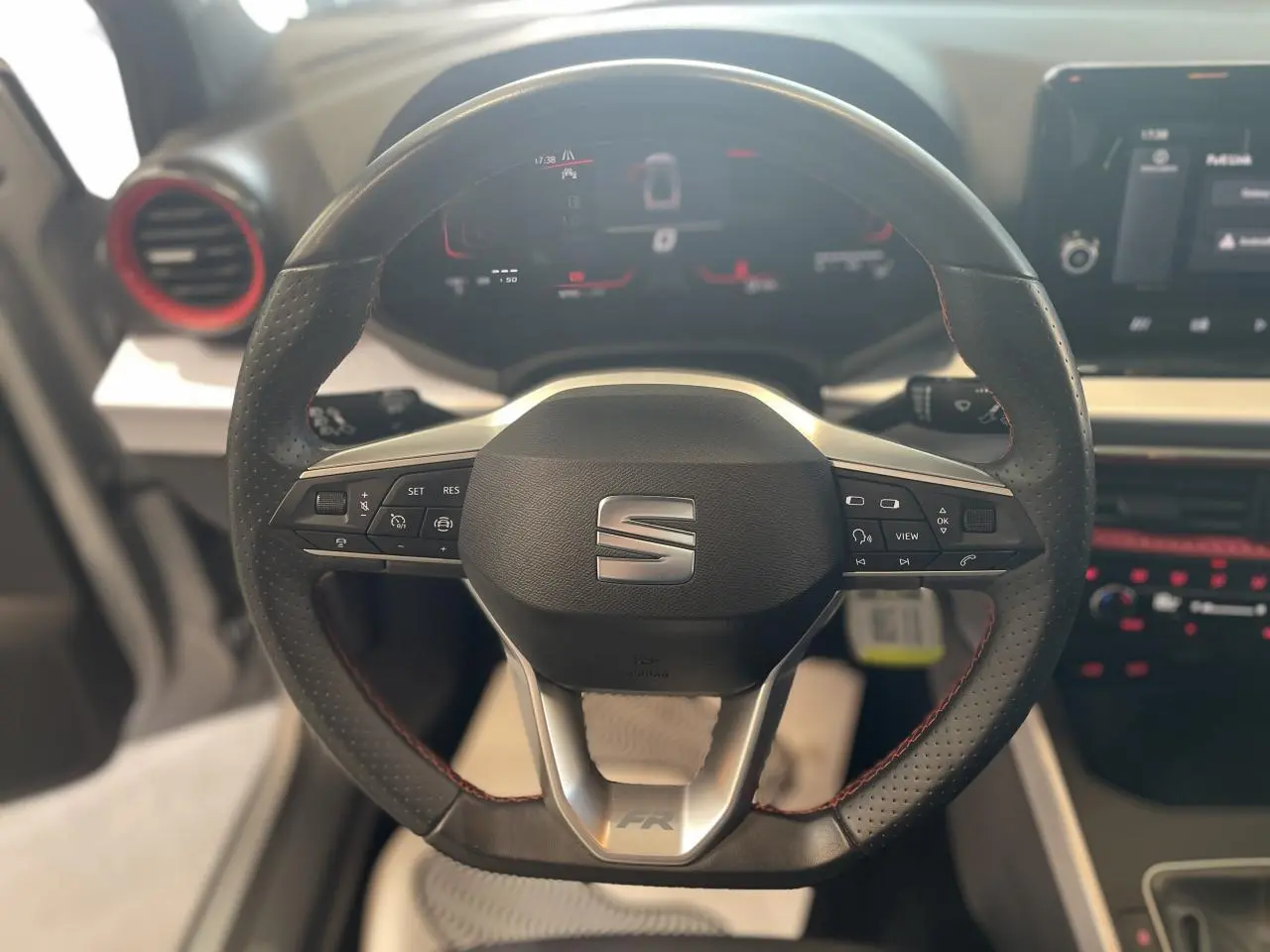 Vue rapprochée du volant sport cuir noir avec logo SEAT et insert FR, tableau de bord digital en arrière-plan.