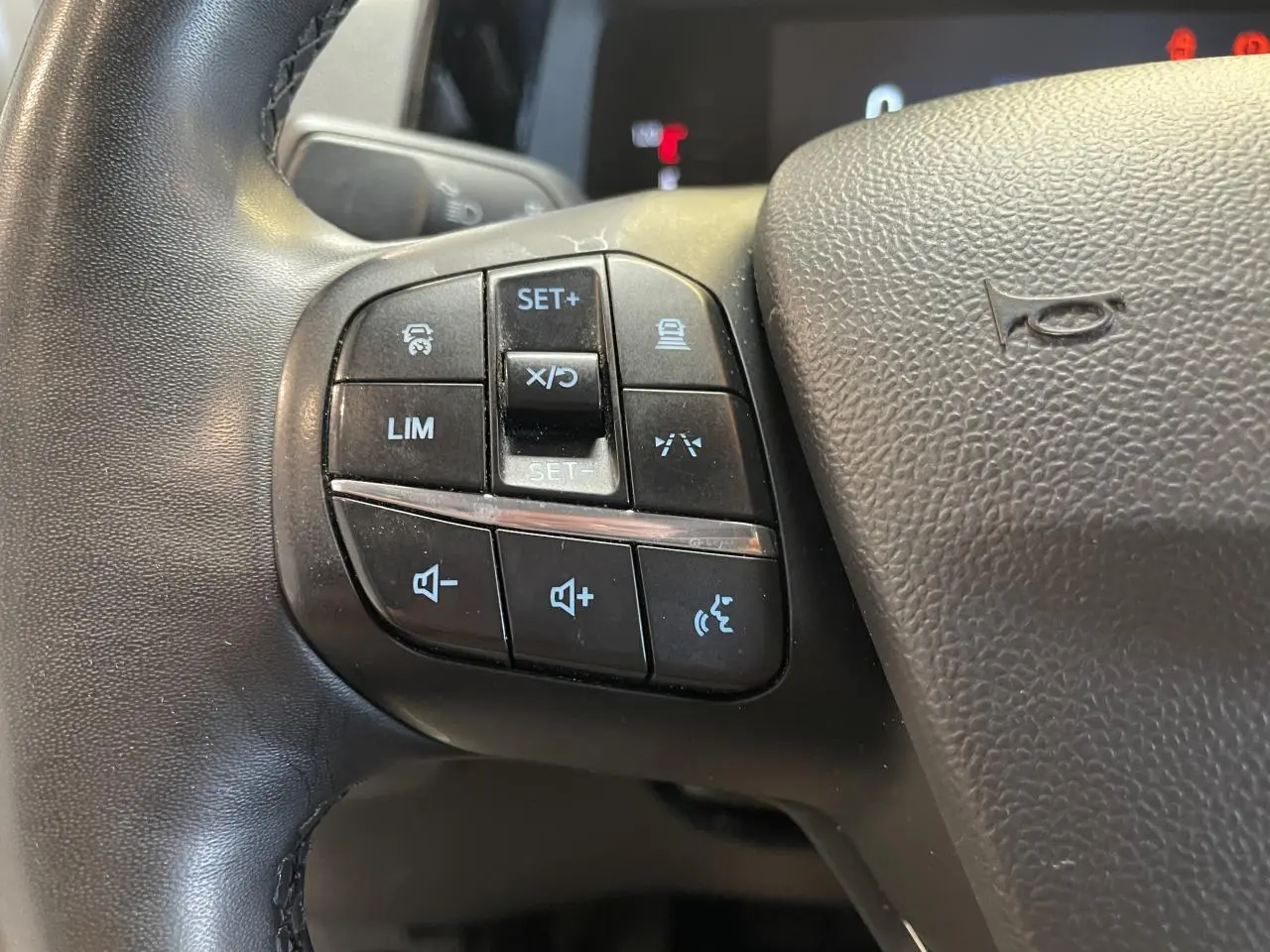 Gros plan sur les commandes multifonctions noires à gauche du volant cuir synthétique du Ford Tourneo Courier gris clair.