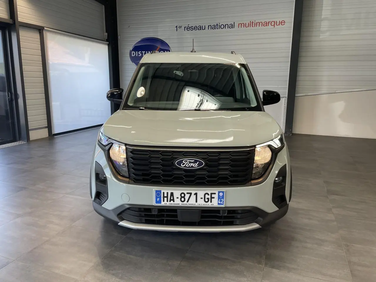 Vue avant du Ford Tourneo Courier gris clair avec calandre nid d'abeille noire et plaques d'immatriculation françaises.