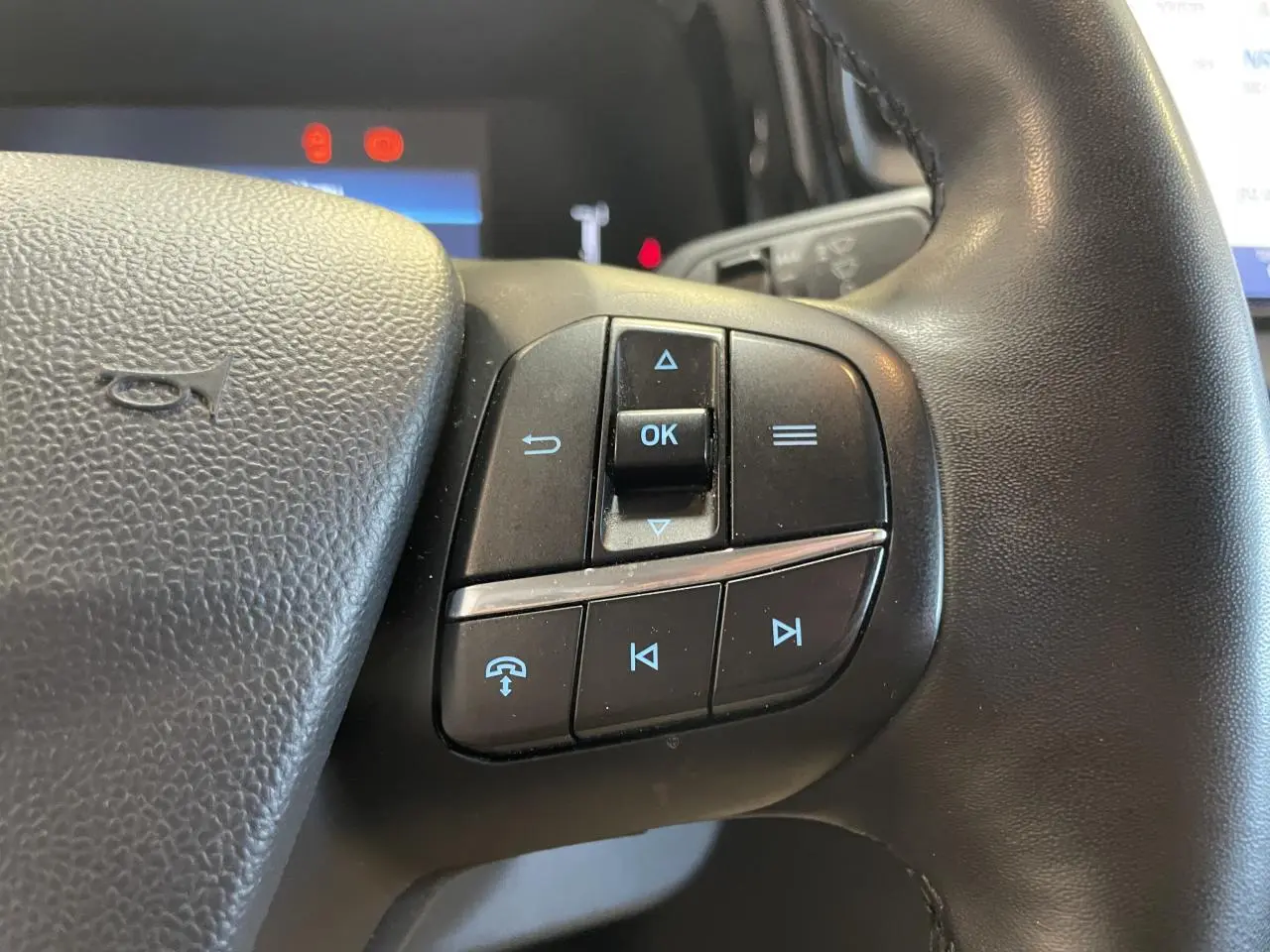 Gros plan sur les commandes multifonctions noires du volant cuir synthétique du Ford Tourneo Courier 2024.