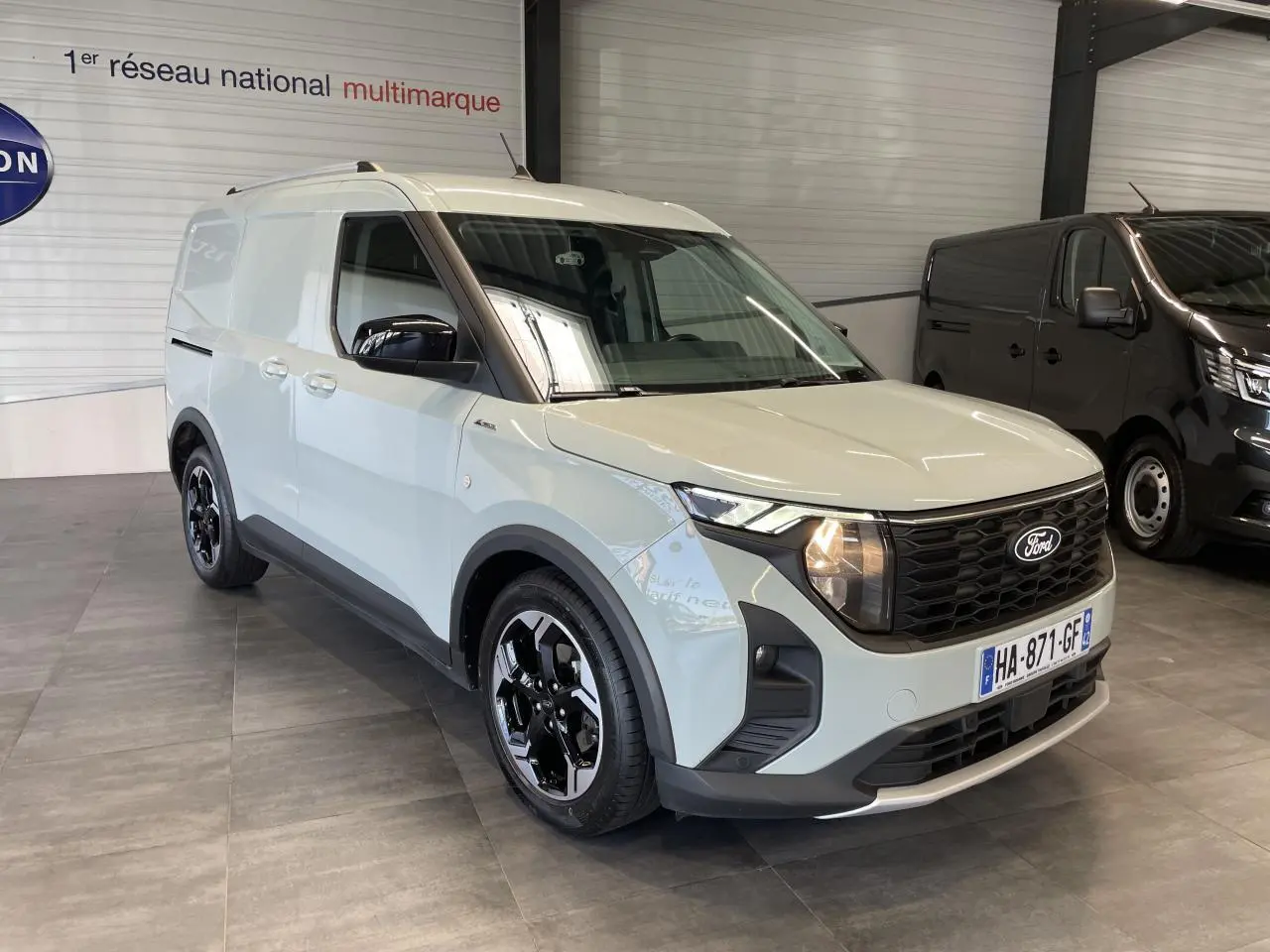 Ford Tourneo Courier gris clair en 3/4 avant droit, avec calandre noire nid d'abeille et jantes alu noires.