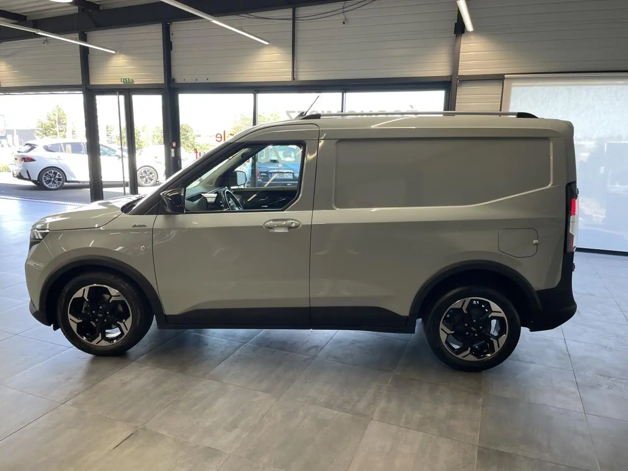 Vue de profil côté gauche du Ford Tourneo Courier 2024 gris clair avec jantes aluminium noires et toit noir.