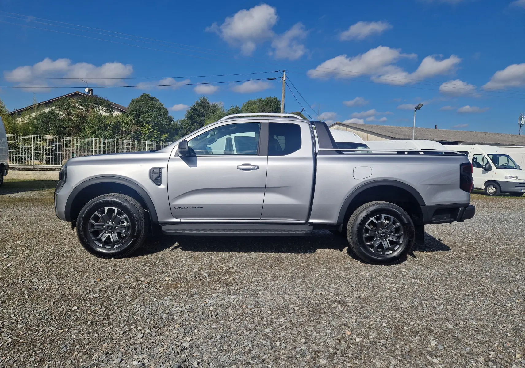 Ford Ranger Wildtrak gris iconic vu de profil côté gauche sur un sol gravillonné avec benne protégée.