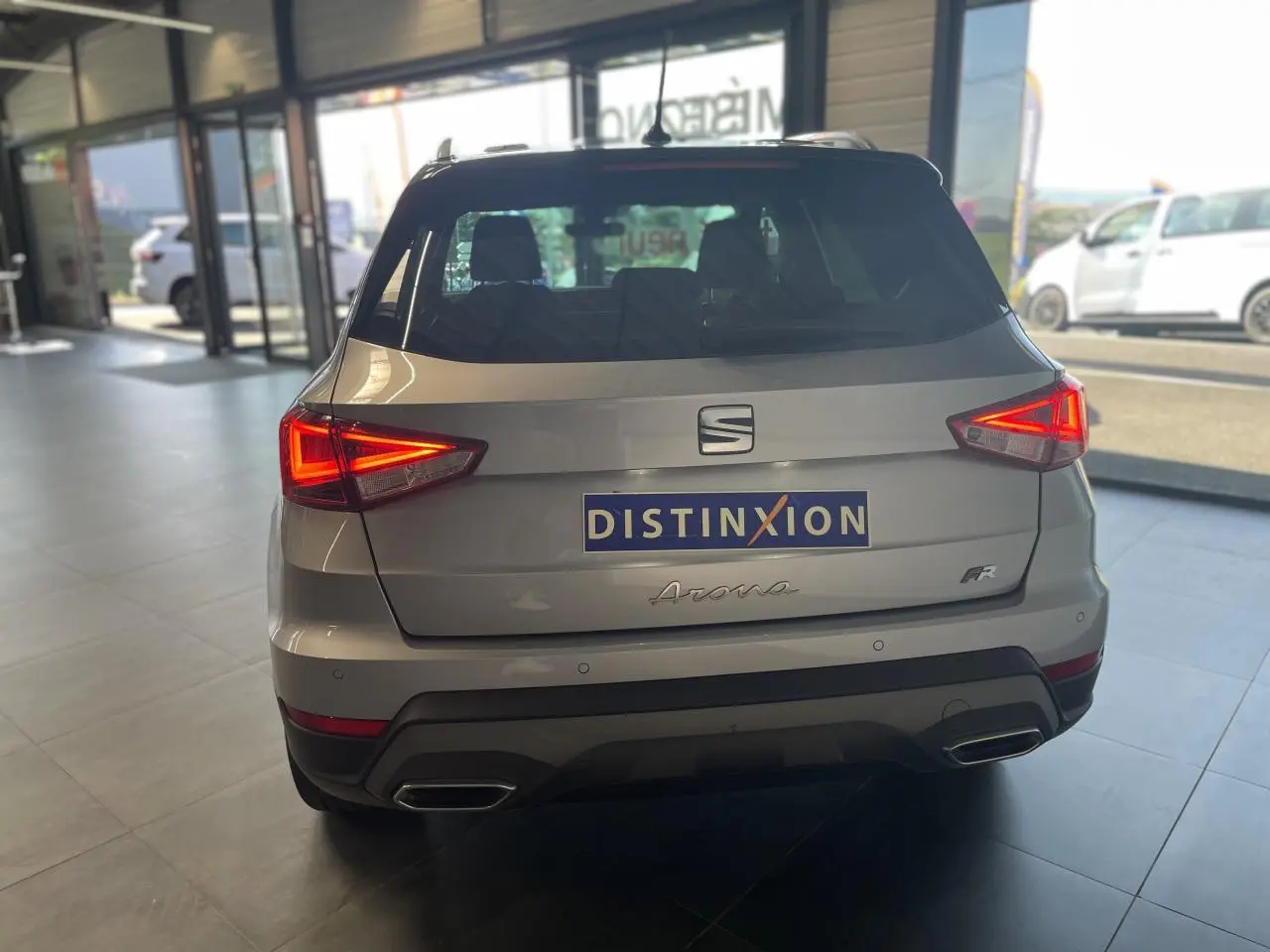 Vue arrière d'un SEAT Arona 2024 gris GRS avec feux allumés et badge FR, en intérieur de showroom.