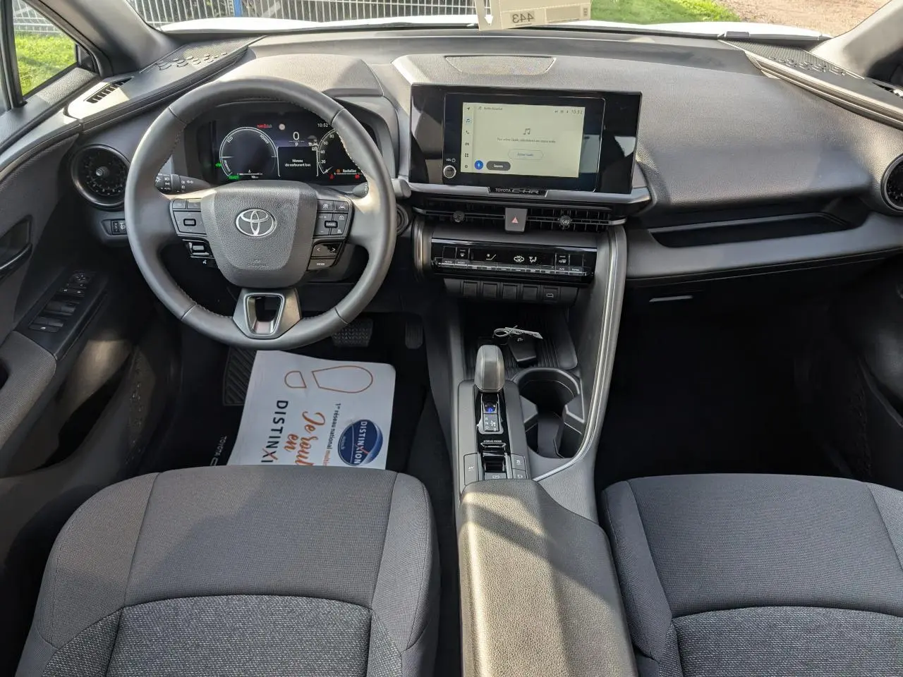 Vue intérieure avant du Toyota C-HR 2024, tableau de bord avec écran tactile 8 pouces et volant multifonction en tissu gris.