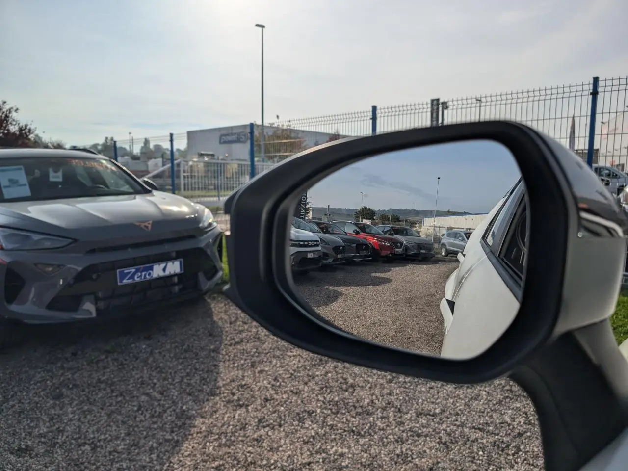 Vue latérale droite du Toyota C-HR blanc 2024, avec rétroviseur reflétant plusieurs voitures en arrière-plan.