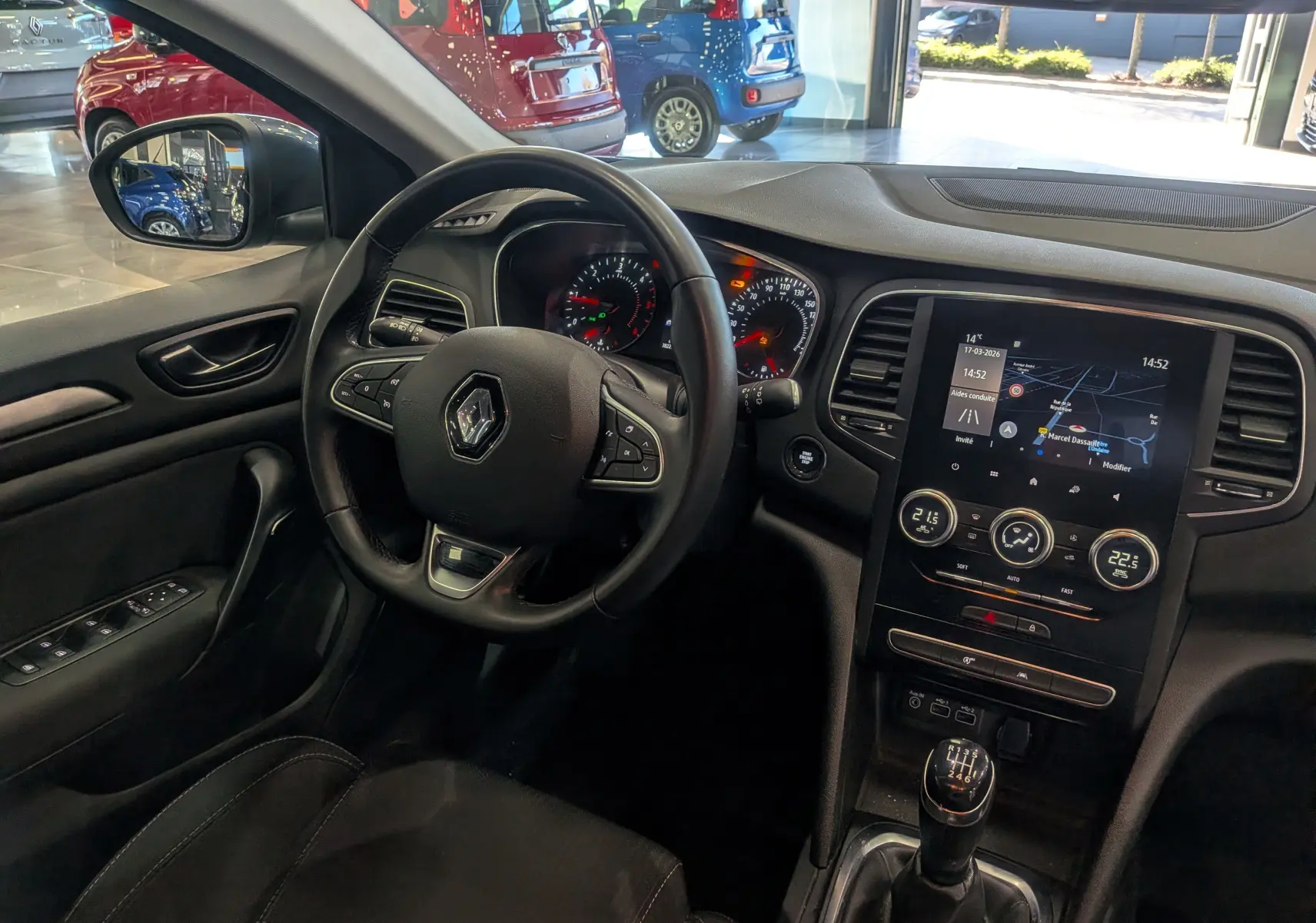 Vue intérieure côté conducteur de la Renault Mégane IV Berline 2022, tableau de bord avec écran tactile et levier de vitesses manuel.