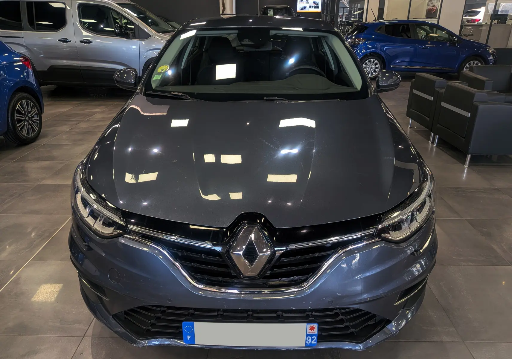 Vue avant d'une Renault Mégane IV Berline gris titanium 2022, avec calandre chromée et logo Renault bien visible.