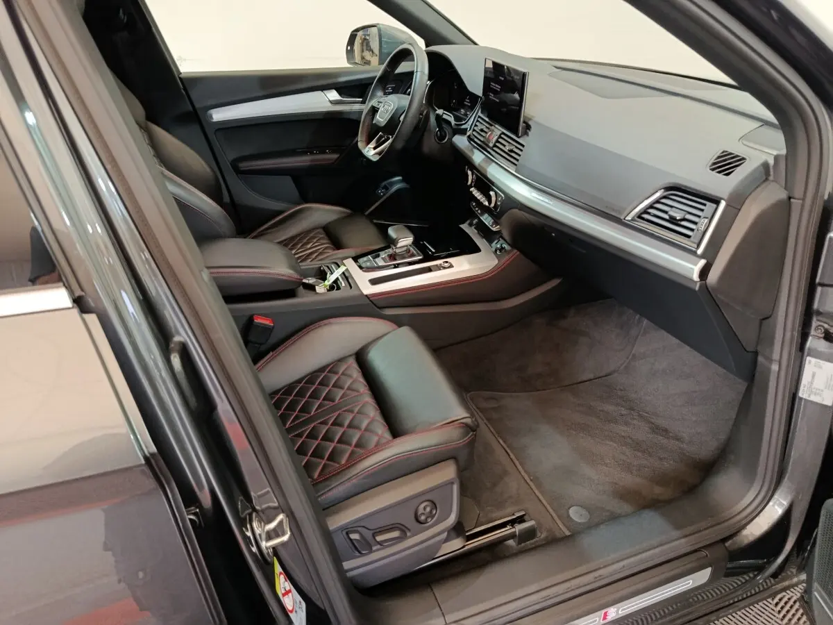 Vue intérieure côté conducteur de l'Audi Q5 2023 hybride rechargeable, sièges cuir noir avec surpiqûres rouges et tableau de bord moderne.
