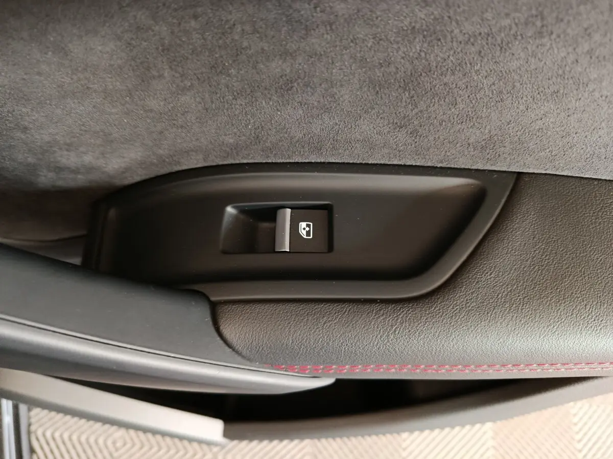 Détail du bouton d'ouverture du coffre sur la garniture intérieure noire avec surpiqûres rouges d'un Audi Q5 gris clair 2023.