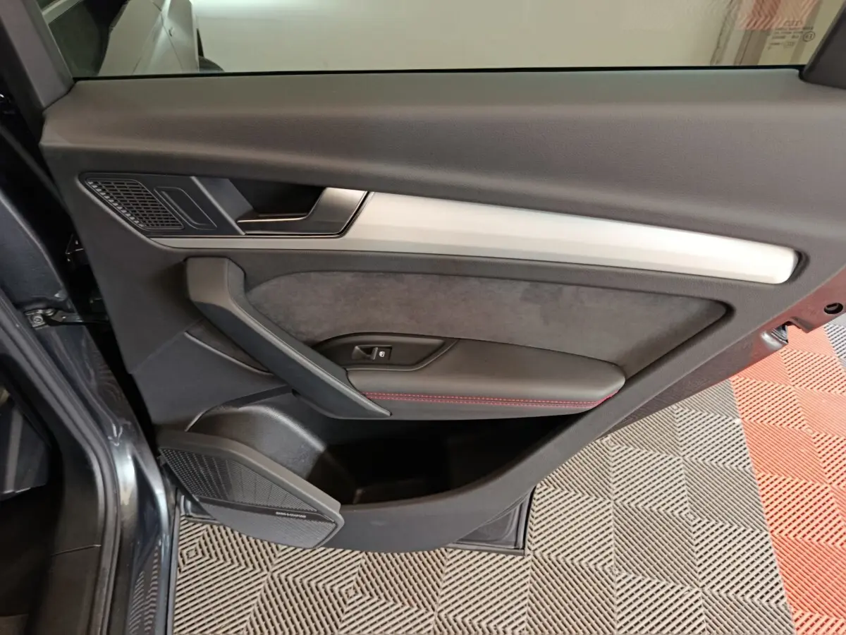 Vue intérieure du panneau de porte côté gauche de l’Audi Q5 2023 gris clair, avec insert en aluminium et haut-parleur Bang & Olufsen.