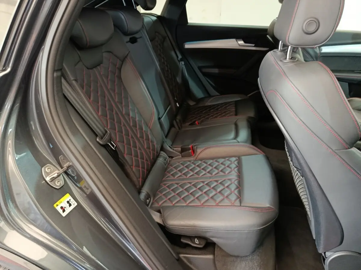 Vue intérieure côté gauche des sièges arrière en cuir noir avec surpiqûres rouges de l'Audi Q5 gris clair 2023 hybride rechargeable.