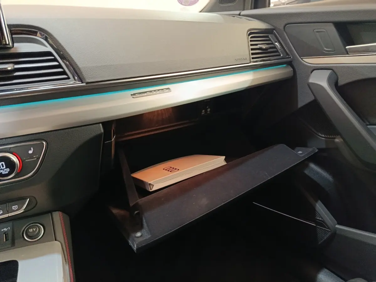 Intérieur de l'Audi Q5 2023 gris clair, vue sur la boîte à gants ouverte côté passager avec manuel Audi visible.