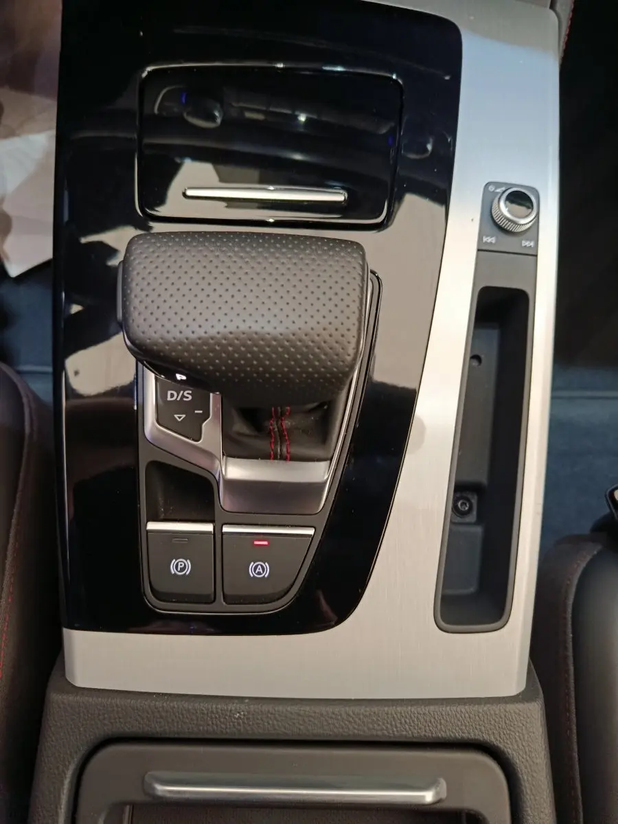 Gros plan sur la console centrale de l'Audi Q5 2023 hybride rechargeable, montrant le levier de vitesses automatique en cuir perforé.