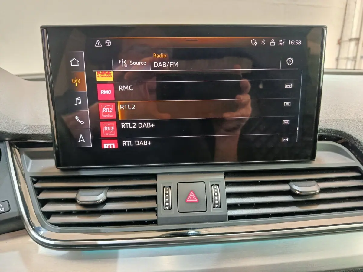Écran central tactile de l'Audi Q5 2023 affichant les options radio DAB/FM, avec commandes d'aération en dessous.