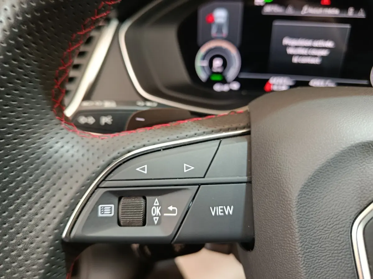 Gros plan sur les commandes gauche du volant perforé avec surpiqûres rouges de l'Audi Q5 hybride rechargeable 2023.
