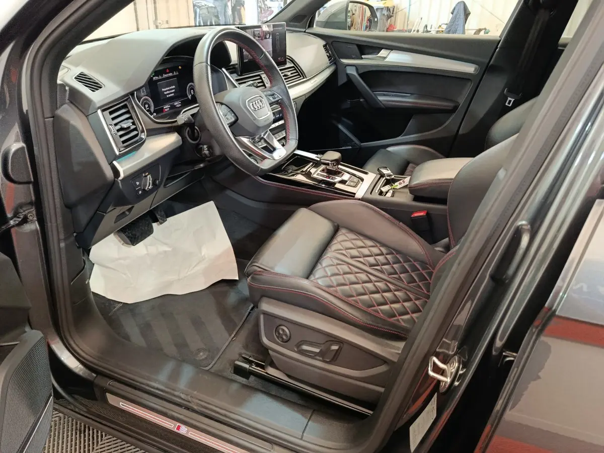 Vue intérieure côté conducteur de l'Audi Q5 2023 gris clair, avec sièges cuir matelassé et volant multifonction.