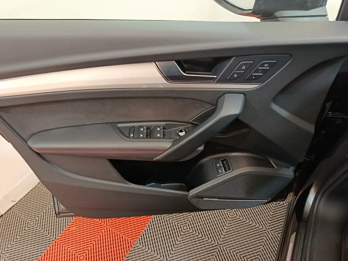 Vue intérieure du panneau de porte côté conducteur de l'Audi Q5 2023 gris clair, avec commandes de vitres et réglages de siège.