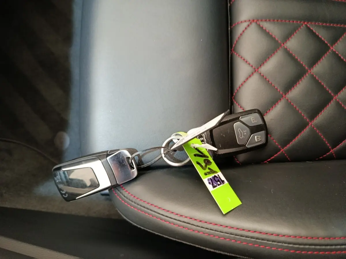 Clé de voiture Audi Q5 2023 hybride rechargeable posée sur un siège cuir noir avec surpiqûres rouges en losange.