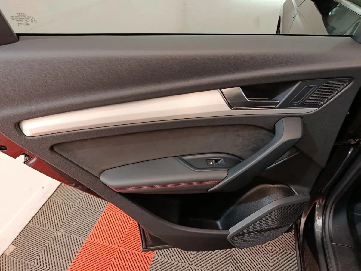 Intérieur de la porte côté gauche de l’Audi Q5 2023 gris clair, avec garniture noire et surpiqûres rouges.