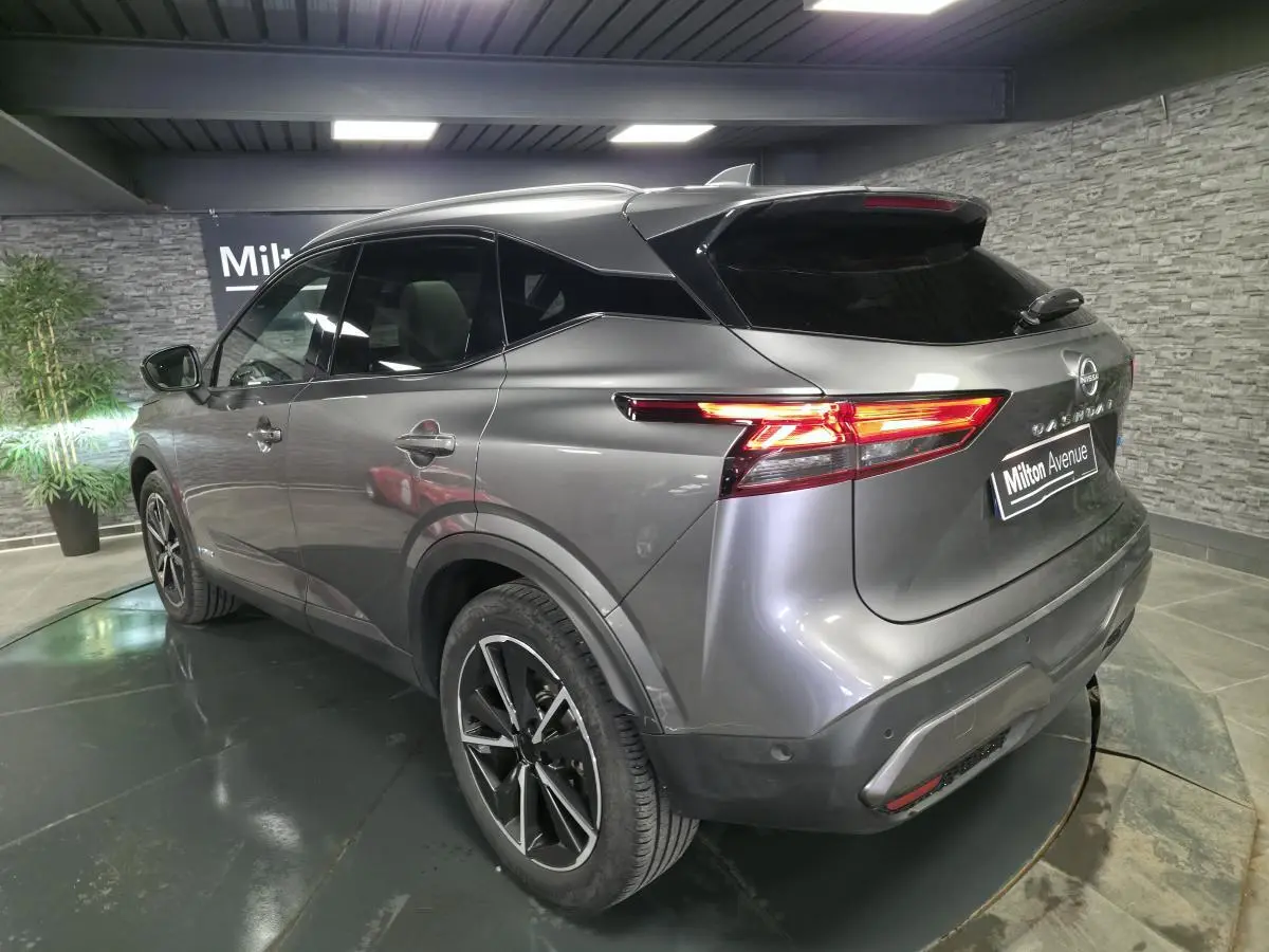 Vue 3/4 arrière droit d'un Nissan Qashqai gris métallisé avec toit noir et feux arrière LED allumés.