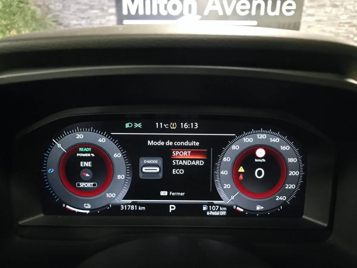 Tableau de bord numérique du Nissan Qashqai gris, affichant le mode de conduite Sport à 16h13.